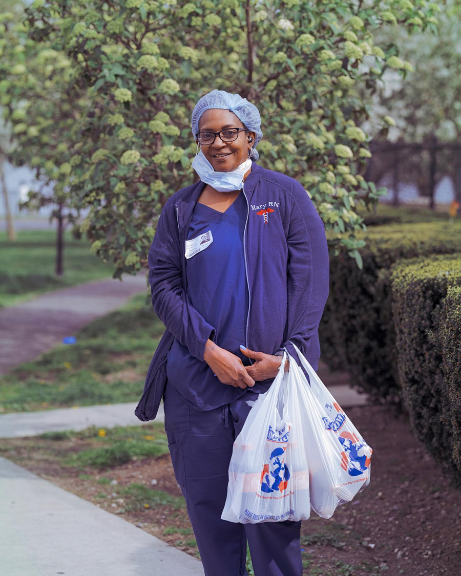 A color photo of an African American nurse wearing blue scrubs, a mask, and a head covering 