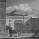 Domed building stands behind fence. Male and female pedestrians stroll along sidewalk in front of building
