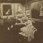 Three men and a woman seated casually around a small table placed in a room filled with framed paintings and sculpture
 