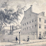 Three-storied building with dormer windows and two front doors stands next to treed lot enclosed by tall fence. Male and female pedestrians stroll along sidewalk