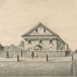 Two large buildings, one topped with cupola and weathervane, stand within busy urban setting. Pedestrians and horse-drawn vehicles visible